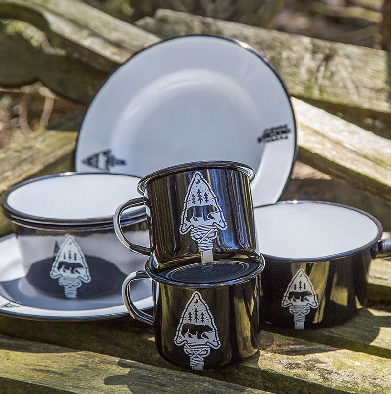 A scene of enamelware featuring a mug, plate, bowl and saucepan in black and white with an arrow and bear logo design on each.