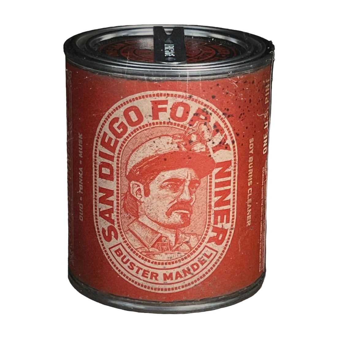 The Buster Mandel San Diego Forty Niner Half Pint Oud Tonka Musk Candle comes in a red tin can adorned with a vintage label featuring an illustration of a man in a helmet. Made with pure soy wax and essential oils, this candle adds an aromatic touch to any space.