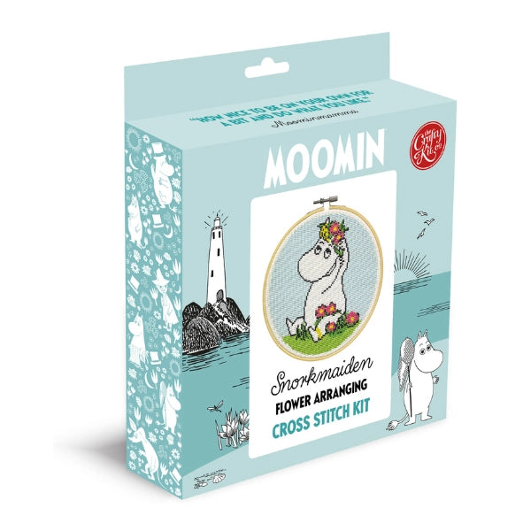 The Crafty Kit Company Snorkmaiden Flower Cross Stitch kit features a pastel blue box with Snorkmaiden arranging flowers on the front and other beloved Moomin characters illustrated on the sides, making it an ideal starter guide for cross stitch beginners.