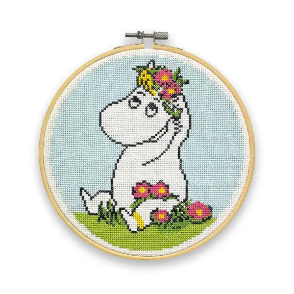 Experience the whimsical charm of The Crafty Kit Company's Snorkmaiden Flower Cross Stitch kit. This delightful cross stitch features the beloved Moomin character, Snorkmaiden, adorned with a flower crown and seated on lush grass, all elegantly framed in an embroidery hoop. It's perfect for adding a touch of magic to your décor!